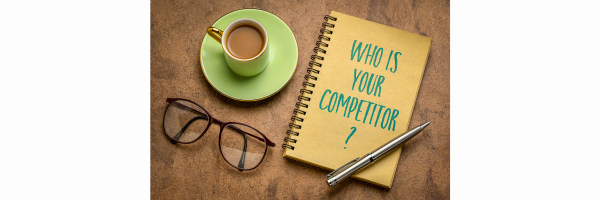 Quién es tu competidor escrito en un cuaderno de espiral junto a una taza y unas gafas