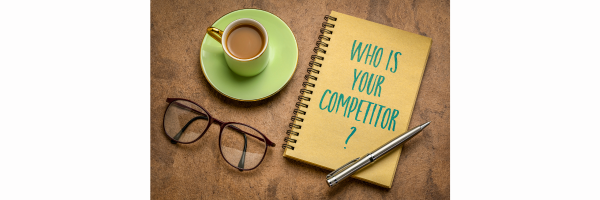 Who is your competitor written on a spiral notepad next to a cup and glasses